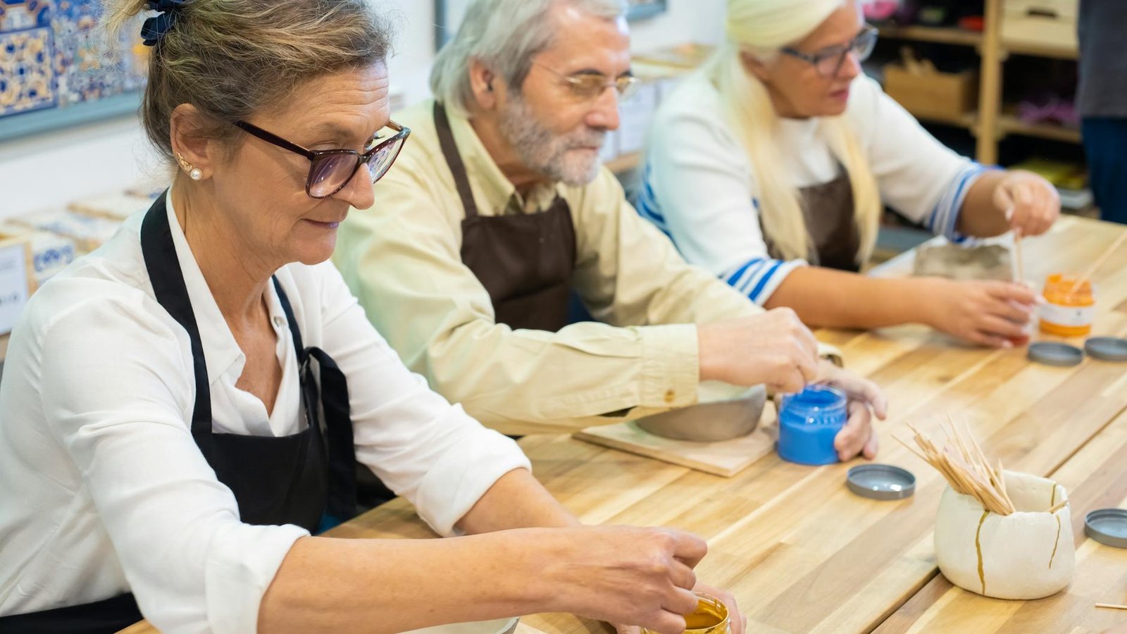 Three older adults focused together in a structured pottery class