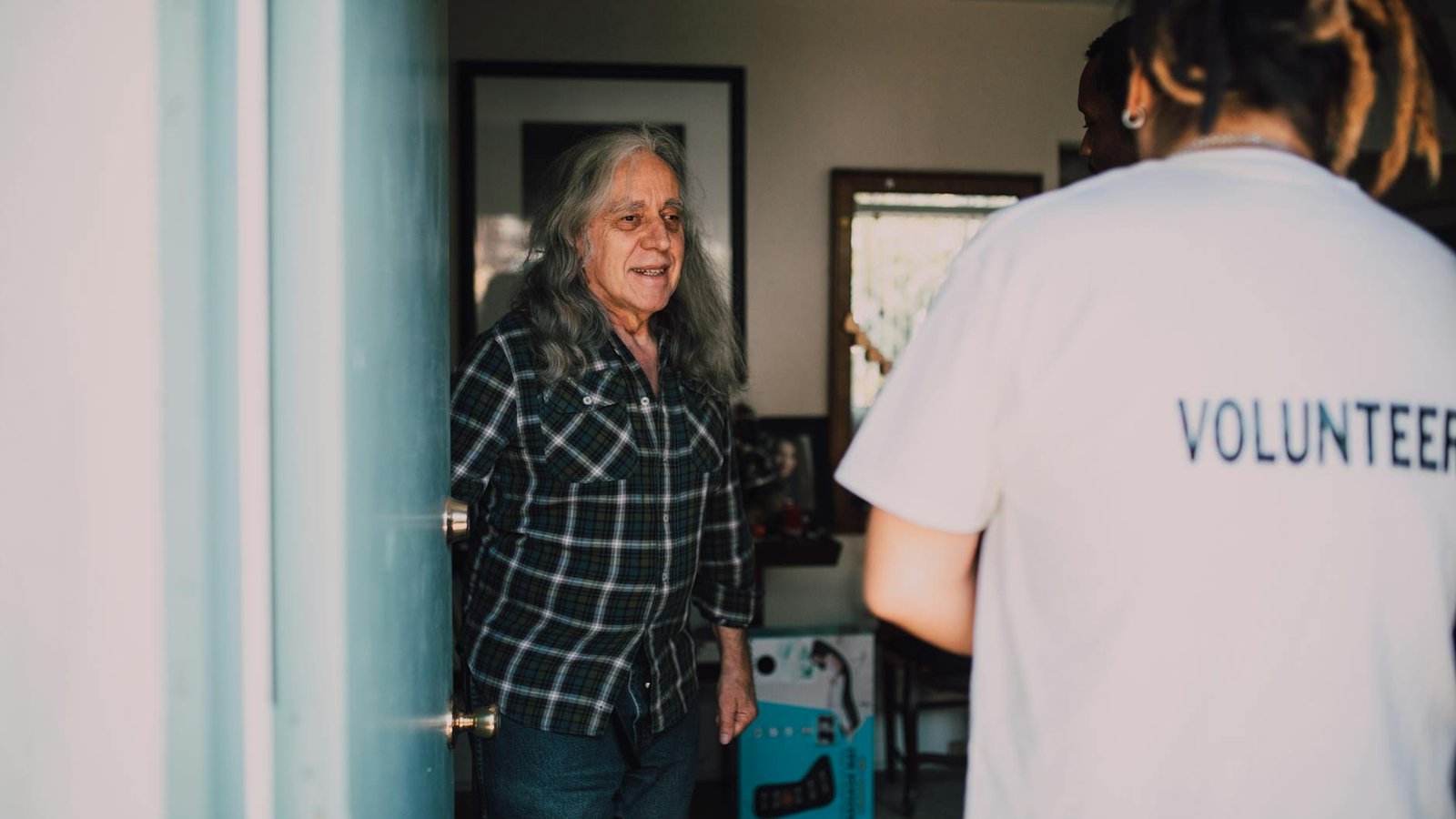 A caregiver greeting an older man at the front door of his home