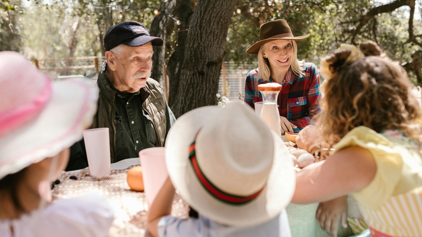 A multigenerational family — grandfather, adult daughter, and grandchildren — sharing a meal outdoors