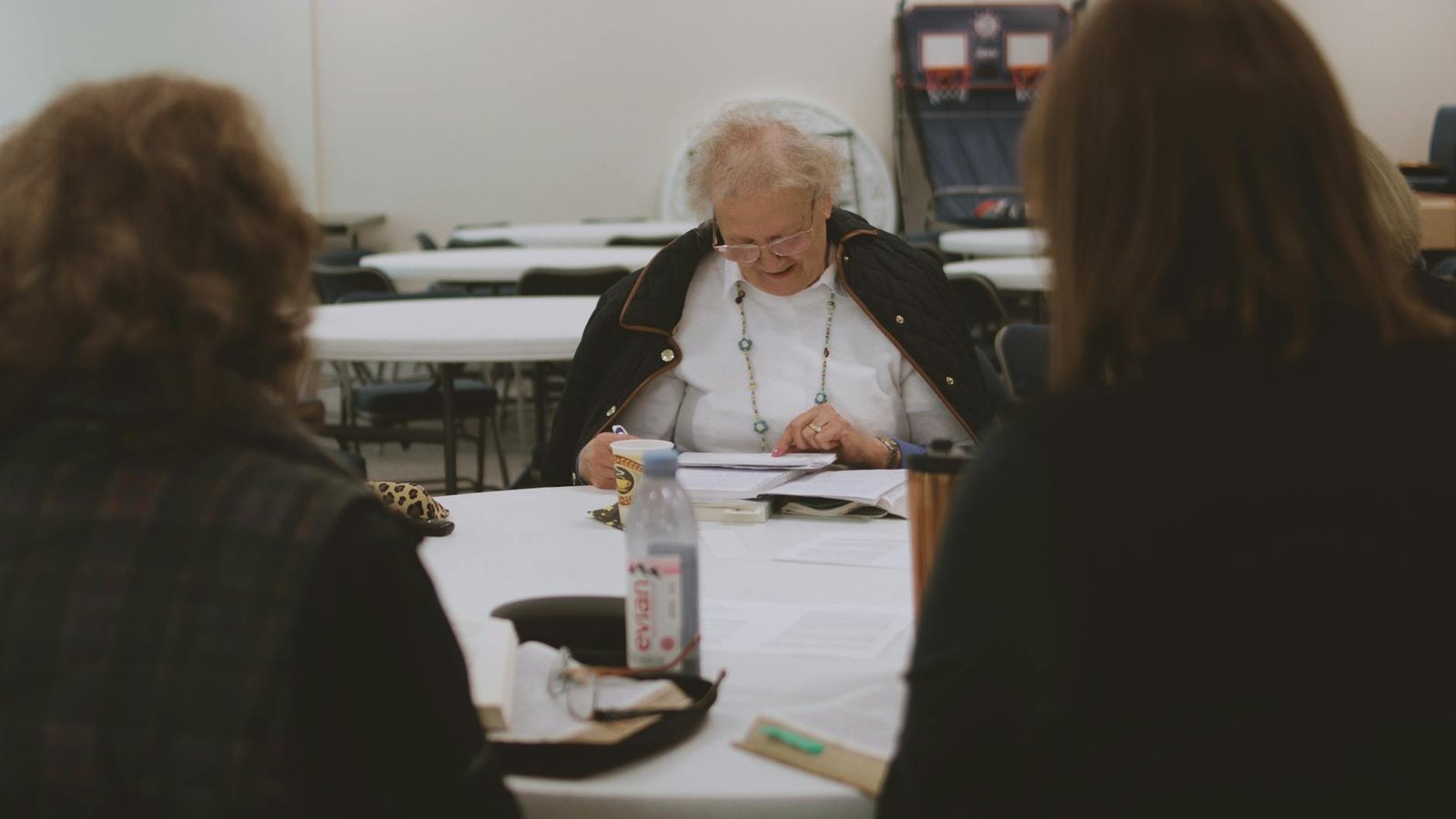 An older woman reading at a communal table in a senior day program setting