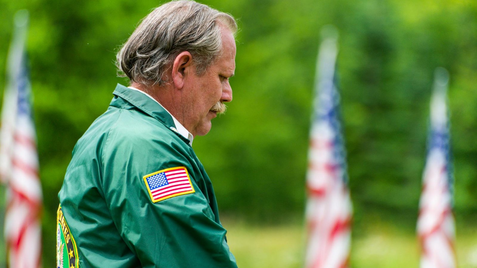 An older US military veteran in a reverent moment surrounded by American flags